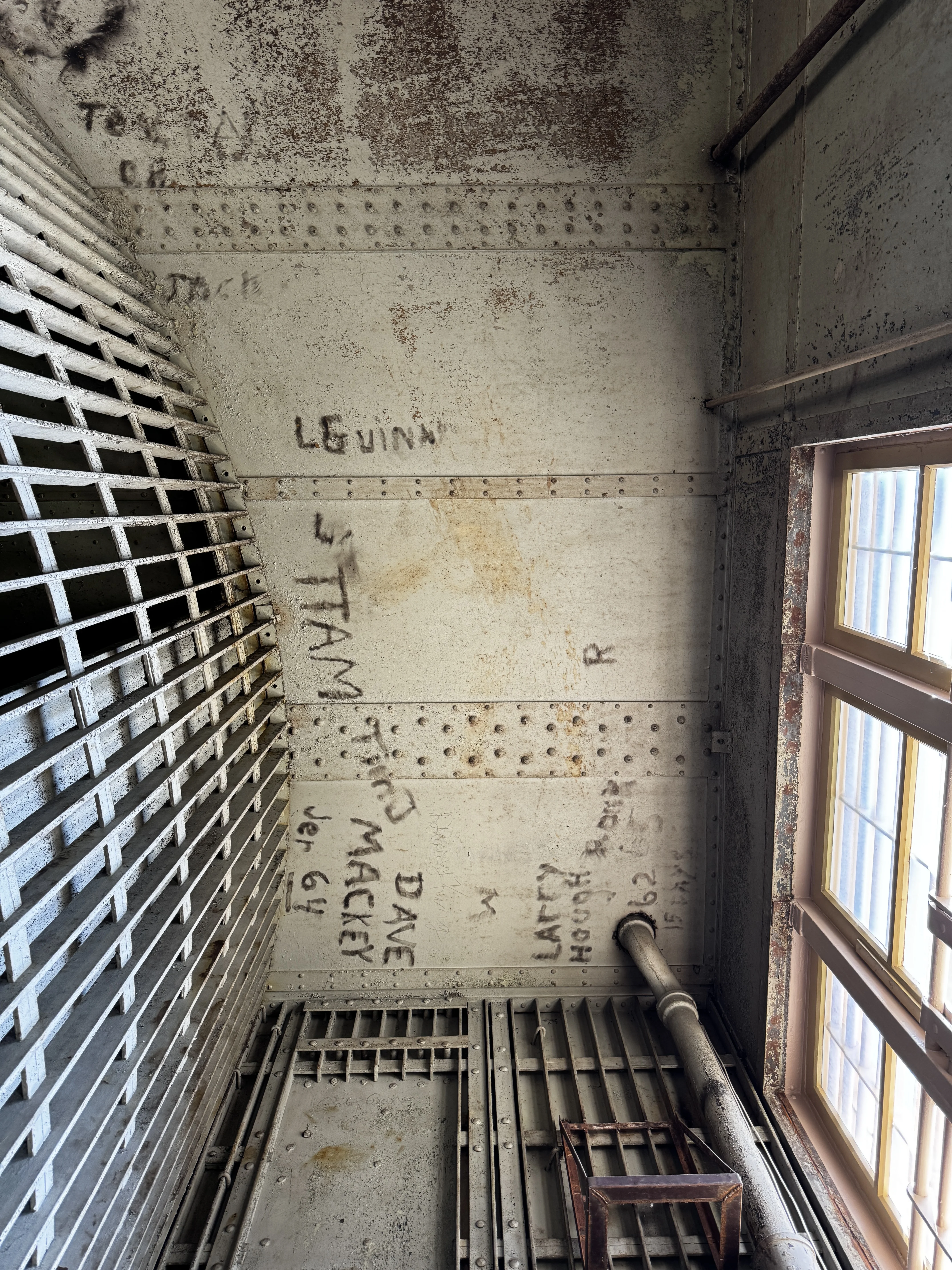 Riveted steel ceiling covered in names and dates carved and painted by prisoners across the mid-twentieth century
